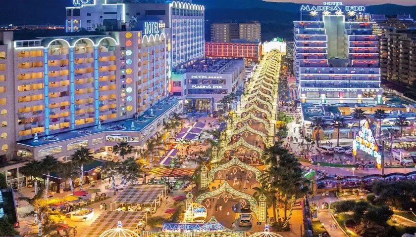 Noche vibrante en Marina d'Or, ciudad de vacaciones, con hoteles iluminados y un paseo lleno de luces y gente.