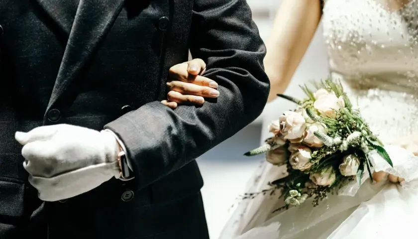 Ojciec prowadzi córkę do ołtarza, trzymając ją pod rękę. Panna młoda w białej sukni z bukietem różowych kwiatów.