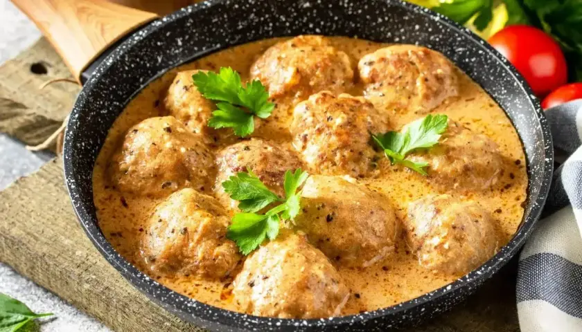 Pulpeciki w kremowym sosie, udekorowane natką pietruszki, gotowe do podania. Pyszny sos do pulpetów kusi aromatem.