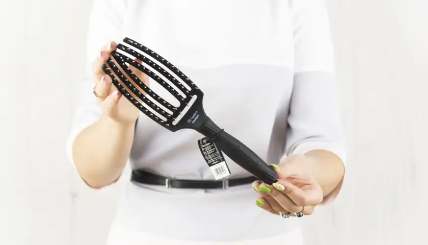 Kobieta trzyma czarną szczotkę do włosów Olivia Garden Fingerbrush.