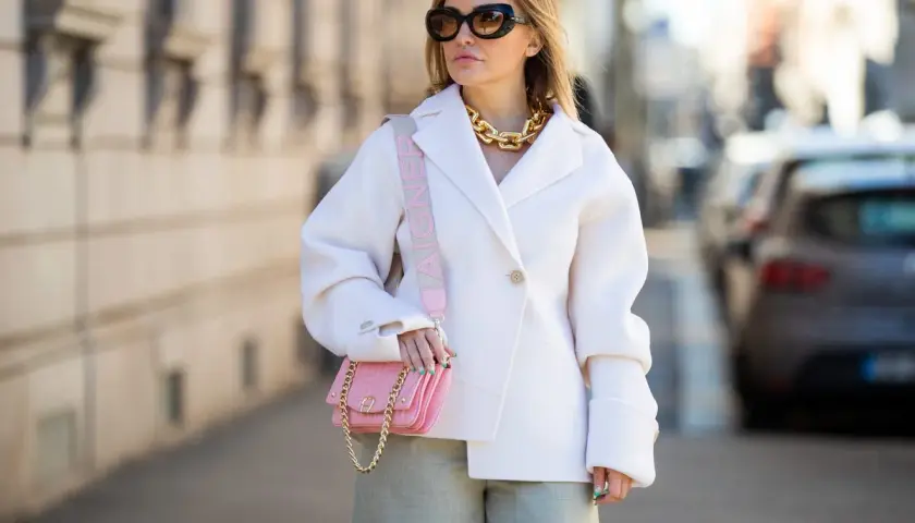 Look para mujeres de 50 años bajitas: abrigo blanco, pantalón verde, bolso rosa y cadena dorada.