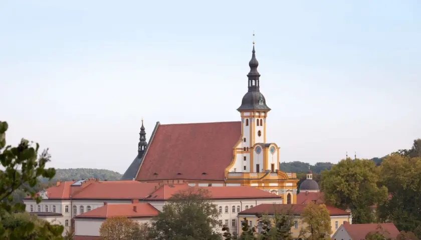 Das Kloster Neuzelle mit seinen roten Dächern und dem markanten Turm, umgeben von Bäumen.