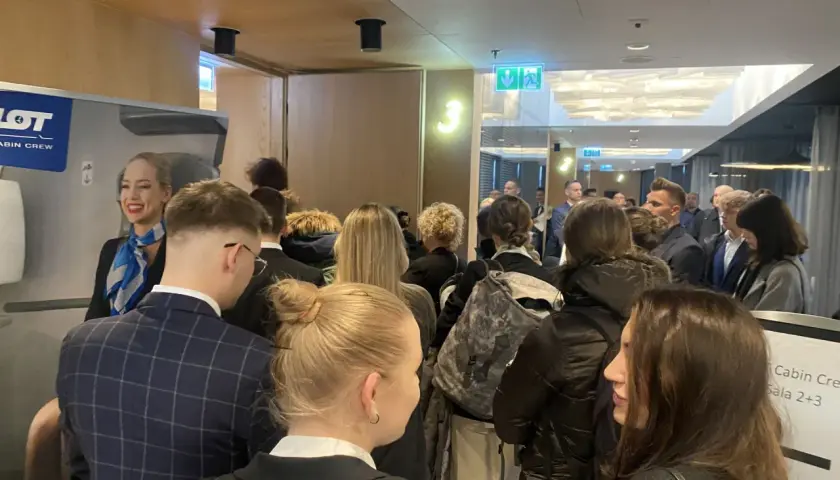 Uśmiechnięta stewardessa LOT Cabin Crew wita grupę osób. Marzenie o pracy w przestworzach zaczyna się tutaj.