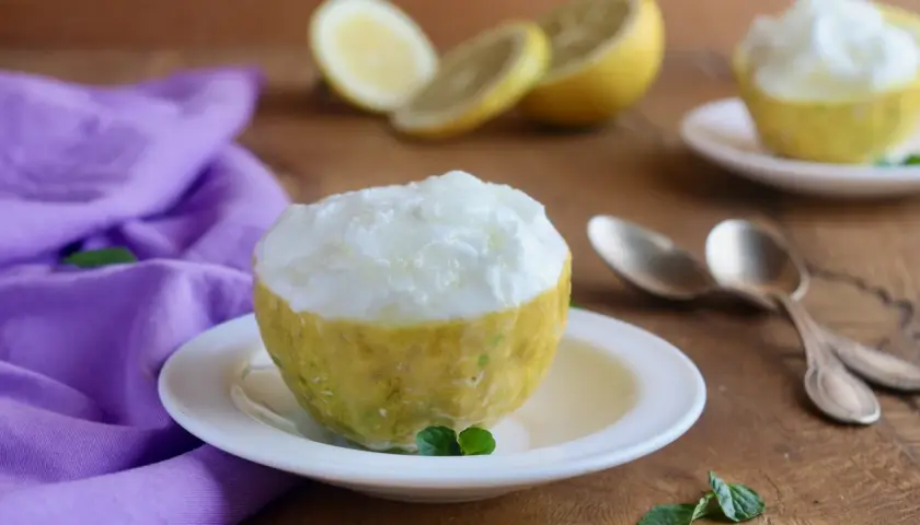 Sorbetto al limone veloce servito in un limone scavato, con limoni affettati e un tovagliolo viola sullo sfondo.