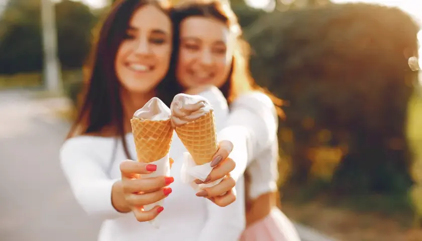 Dwie uśmiechnięte dziewczyny trzymają lody w wafelkach. Czy lody tuczą? Może odrobina przyjemności nie zaszkodzi!