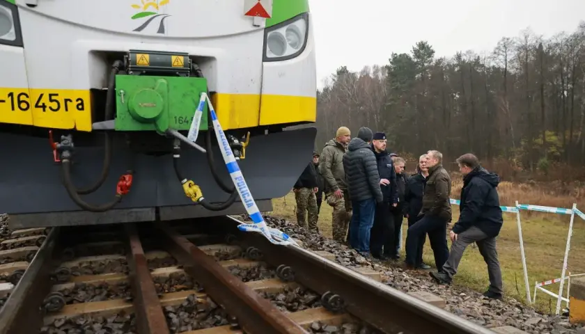 Grupa osób, w tym policjanci, ogląda przód lokomotywy EU07 005, otoczony taśmą policyjną.