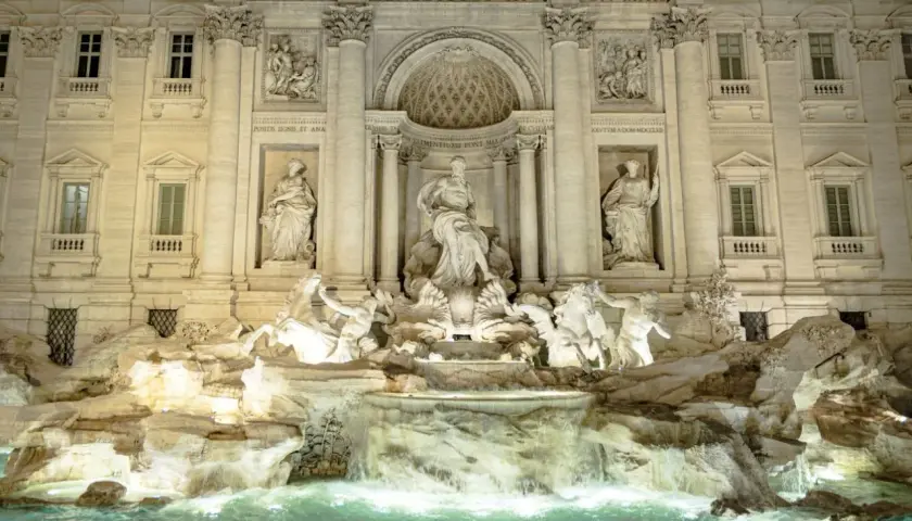 Trevi Fountain at night, with illuminated sculptures and cascading water.