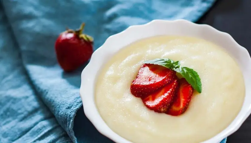 Gładka kaszka manna, czyli semolina co to, podana z truskawkami i miętą na niebieskim tle.