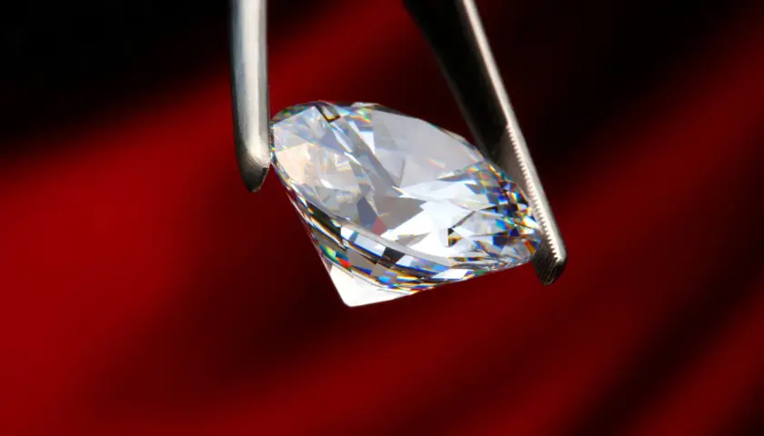 Ein funkelnder Diamant, gehalten von einer Pinzette, zeigt sein gesamtes Spektrum an Farben. Was ist ein brillant? Ein Stein, der Licht bricht und verzaubert.