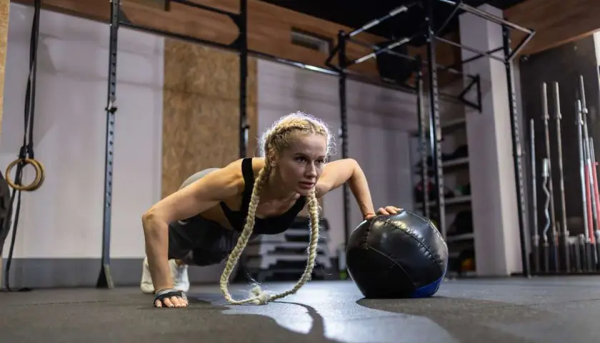 Kobieta w pozie pompki z piłką treningową, idealne ćwiczenie na początek przygody z crossfit.