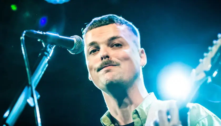 Blazej Krol śpiewa do mikrofonu, trzymając gitarę.