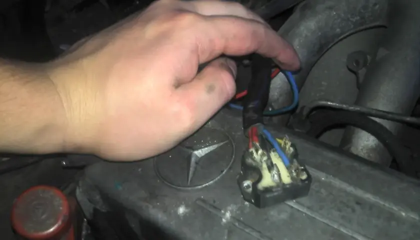 Ręka majstruje przy kostce elektrycznej, by sprawdzić wentylator nawiewu na krótko. Widoczny przekaźnik i przewody.