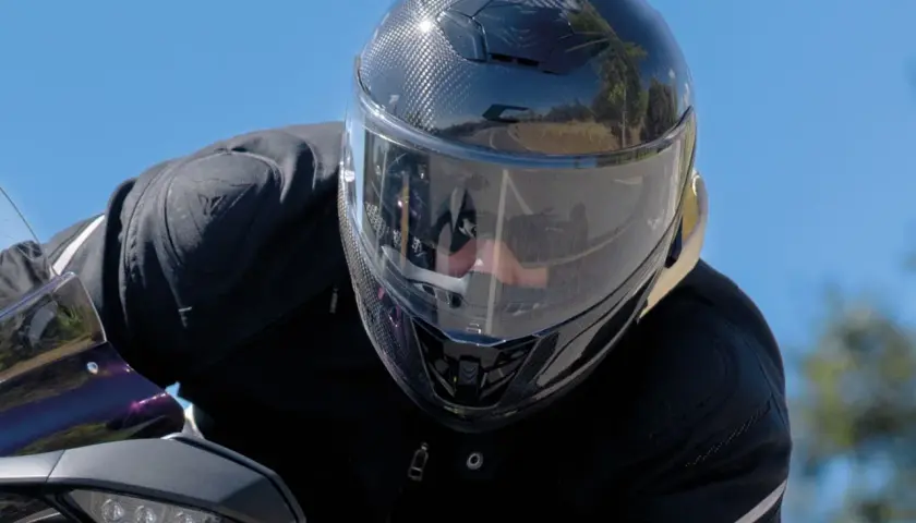 Motociclista con un casco mas silencioso de fibra de carbono, disfrutando del paisaje en un día soleado.