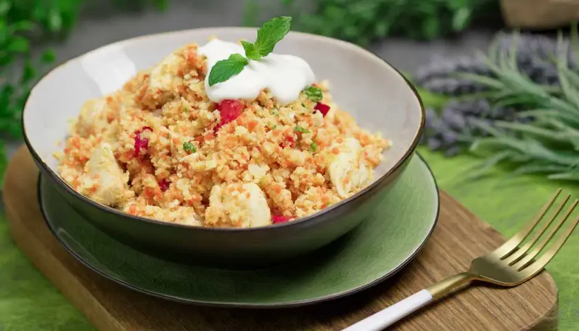 Schüssel mit Hähnchen und buntem Gemüse, garniert mit Joghurt und Minze. Ein köstliches Gericht, das zeigt, dass ist Couscous low carb möglich ist.