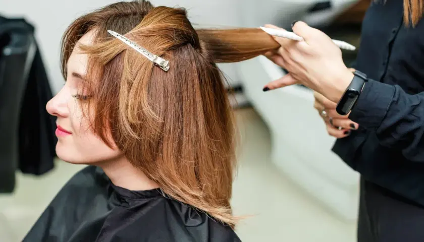 Kobieta z brązowymi włosami do ramion, fryzjerka modeluje pasmo włosów.