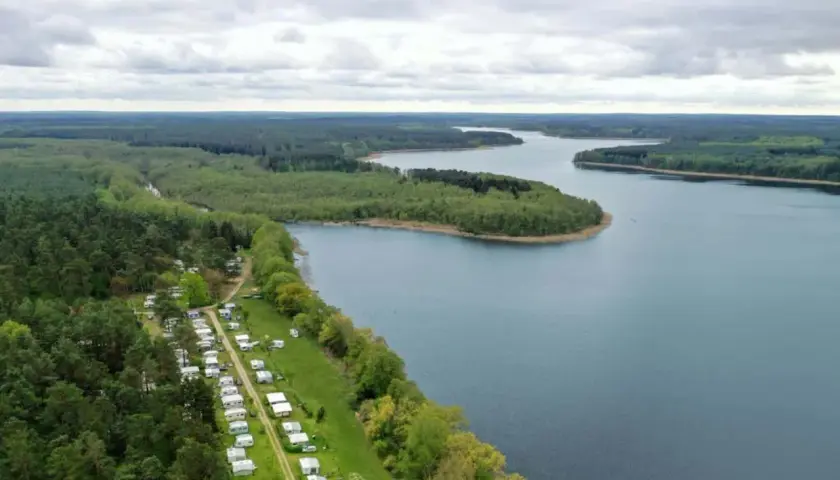 Vue aérienne d'un camping naturiste en Allemagne, bordé par une forêt dense et un lac paisible.