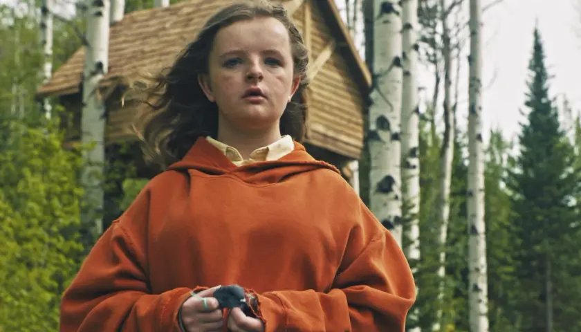 Charlie i orange hoodie, med en fågel i händerna, framför ett trädkoja i skogen. En scen från rollistan i Hereditary.