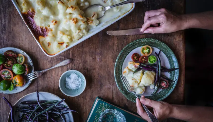 En härlig gratinerad blomkål i en ugnsform, serverad med färska grönsaker och en bok.