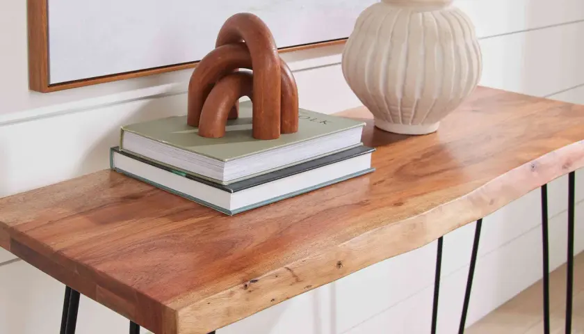 A live-edge acacia hardwood console table displays books, a wooden sculpture, and a textured vase.