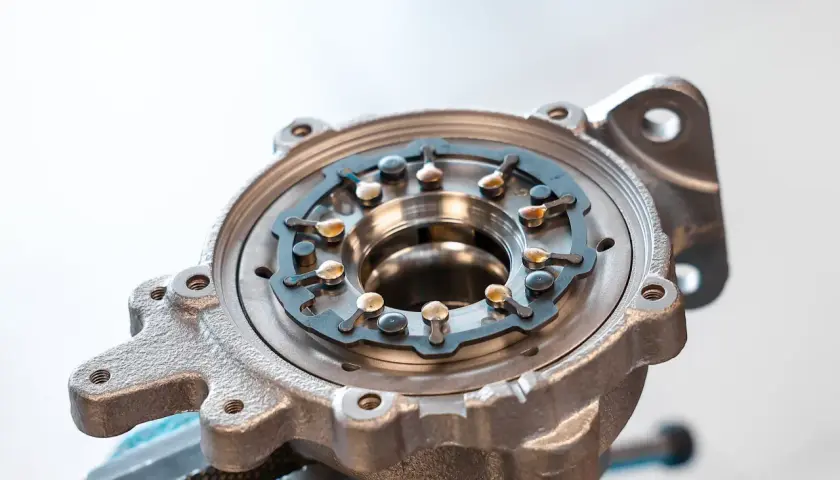 Metalowa obudowa turbo ze zmienną geometrią, z widocznymi łopatkami i mechanizmem regulacji.