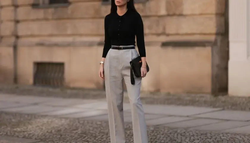 Elegancka stylizacja na imprezę dla 40-latki: czarny top, szare spodnie z wysokim stanem, czarna torebka i okulary.