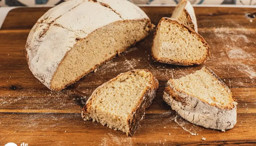 Un pan de papa casero, con su corteza dorada y miga esponjosa, cortado en rebanadas sobre una tabla de madera.