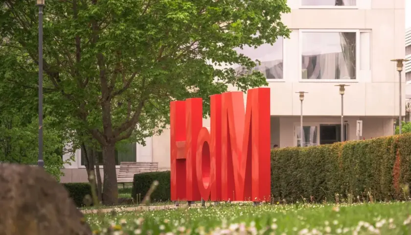 Große rote Buchstaben "HdM" vor einem Gebäude. Hier könnte dein berufsbegleitendes Studium in Stuttgart beginnen.