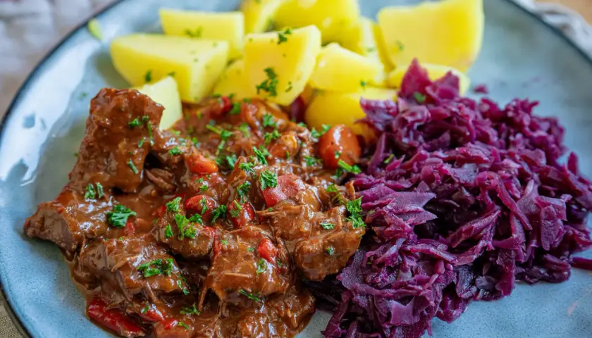 Herzhaftes Gulasch, ein typisches Gericht für schmorgerichte im ofen, serviert mit Salzkartoffeln und Rotkohl.