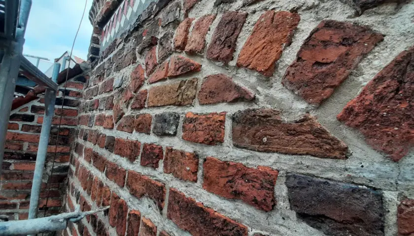 Różne rodzaje cegieł tworzą starą, czerwoną ścianę. Widać nierówności i ślady czasu na cegłach.