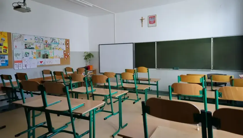 Pusta klasa szkolna z rzędami ławek i krzeseł. Na ścianie tablica, projektor i dziecięce rysunki. Odwołane zajęcia w szkołach sprawiają, że sale wyglądają tak.