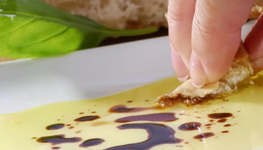 Ein Stück Brot wird in Olivenöl mit Balsamico getunkt. Eine Frau genießt diesen Snack, vielleicht während der Schwangerschaft.