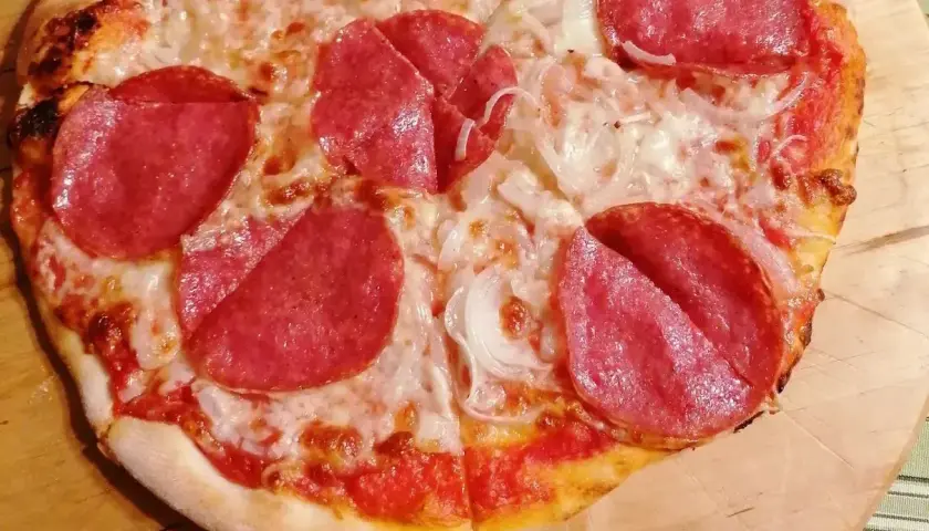 Pizza z salami i cebulą. Salami, czyli wędlina z mielonego mięsa wieprzowego, jest głównym składnikiem tej pysznej pizzy.