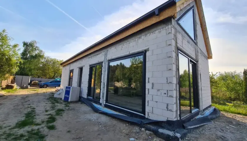Nowy dom w stanie surowym zamkniętym, z dużymi oknami i dachem.