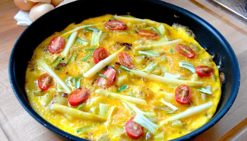 Omelette aux asperges vertes et oignons, garnie de tomates cerises, prête à être dégustée. Une recette simple et savoureuse.