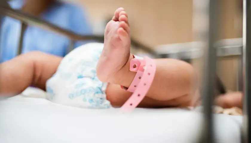 Ett litet barns fot med ett rosa armband, kanske en nyfödd bebis. Vad betyder bb? En ny början.