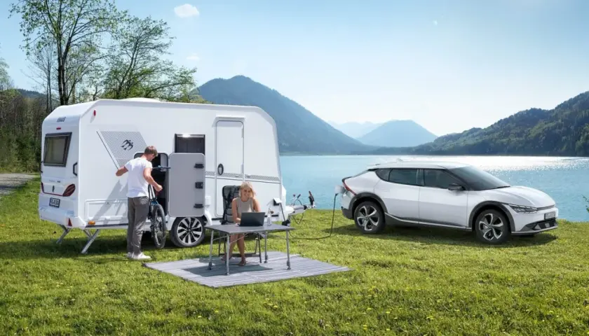 Para wakacyjna z przyczepą kempingową i ładowanym autem elektrycznym nad jeziorem. Idealne na wycieczkę z prawem jazdy B96.