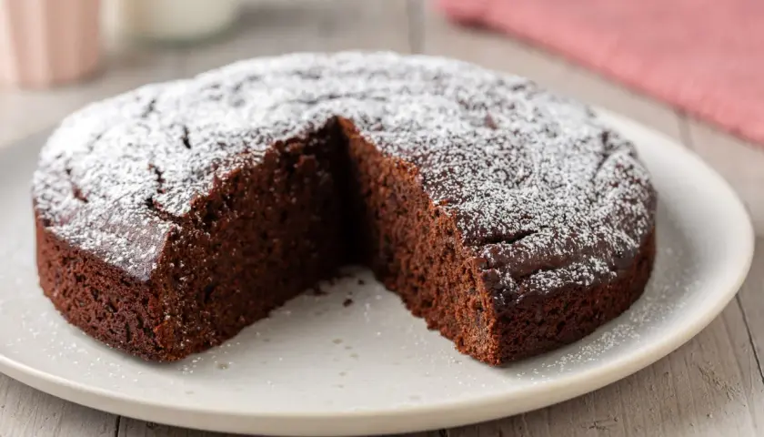 Una fetta è stata tolta da questa torta al cioccolato soffice, cosparsa di zucchero a velo.