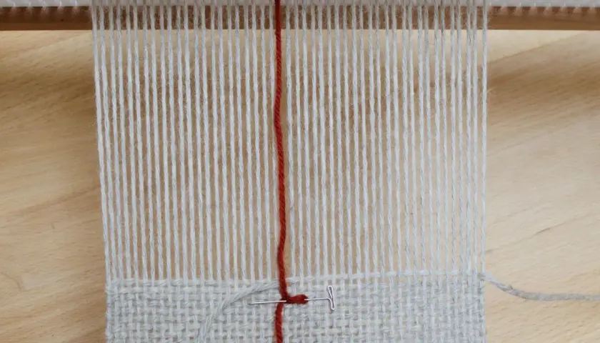 Début d'un tissage sur métier, fils de coton gris et rouge. La technique de tissage se révèle avec chaque passage.