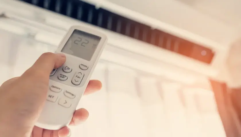 Mano ajustando el control remoto del aire acondicionado, mostrando la temperatura a 22 grados. ¿Qué potencia de aire acondicionado necesito para mi hogar?