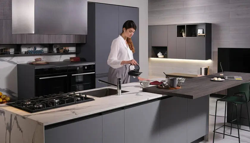 Donna prepara il tè in una moderna isola cucina fai da te con piano in marmo e bancone snack.