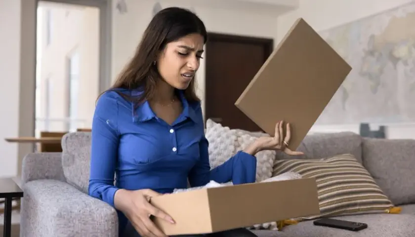 Femme déçue ouvrant un colis, découvrant un produit non conforme à la commande. Elle exprime son mécontentement.
