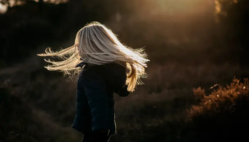 Dziecko z rozwianymi blond włosami w świetle zachodzącego słońca.