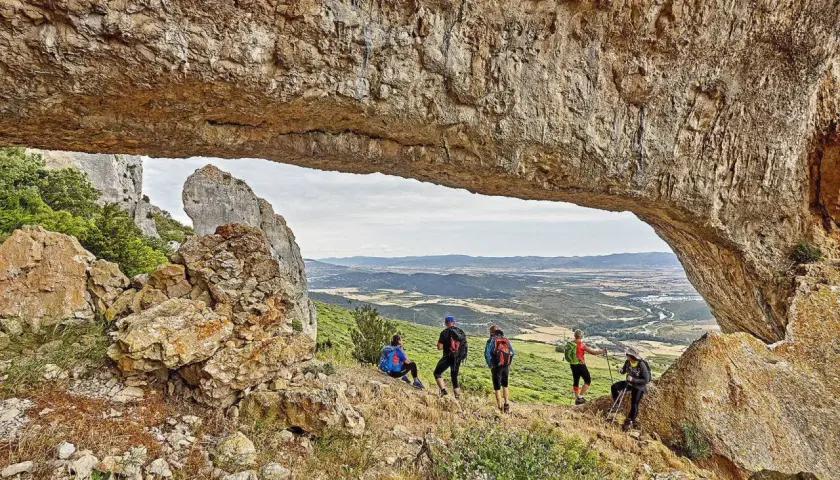 Senderistas disfrutan de vistas panorámicas en rutas por Navarra, bajo un arco natural de roca.