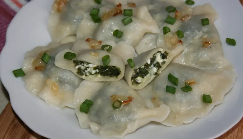Pyszne pierogi ze szpinakiem i serem, posypane szczypiorkiem i skwarkami. Idealne na obiad!