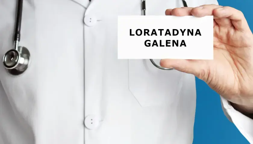Lekarz trzyma kartkę z napisem "LORATADYNA GALENA". Stetoskop wisi na jego białej katanie.