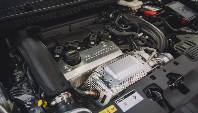 Silnik 1.6 PureTech z napisem "PEUGEOT SPORT" na metalowej osłonie. Widać turbosprężarkę i elementy układu dolotowego.