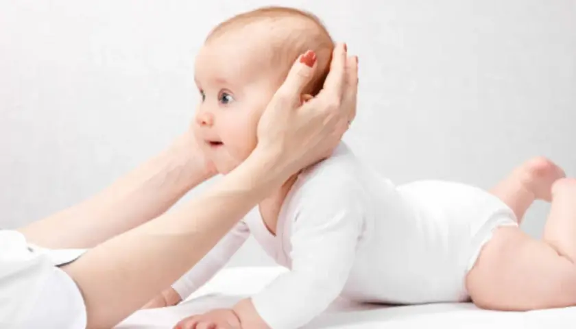 Manos sostienen la cabeza de un bebé que gatea. ¡Qué lindo mi bebe se pega en la cabeza!