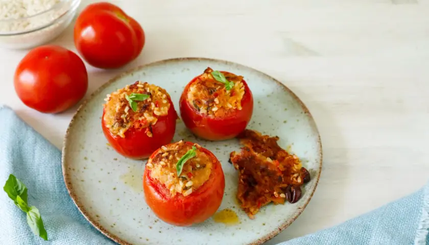 Pomodori ripieni tonno e riso, guarniti con basilico, su un piatto con un contorno croccante.