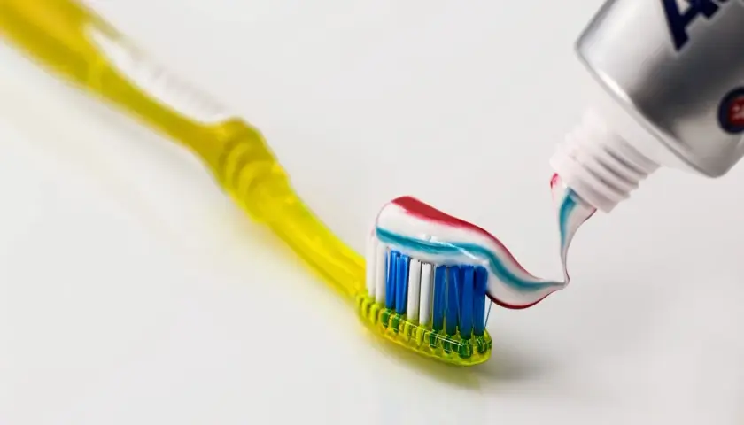 Żółta szczoteczka do zębów z kolorową pastą wyciskaną z tubki.