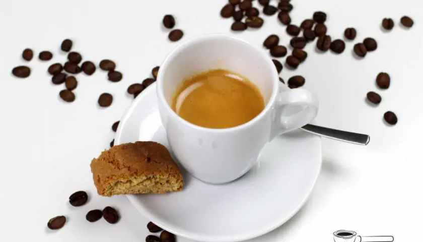 Ein weißer Becher mit Kaffee, daneben ein Cantuccini und Kaffeebohnen. Das ist ein Kaffee Lungo, ein längerer Espresso.